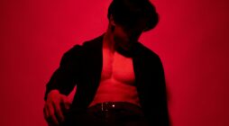 Studio portrait of a muscular man in dramatic red lighting, conveying strength and mystery.